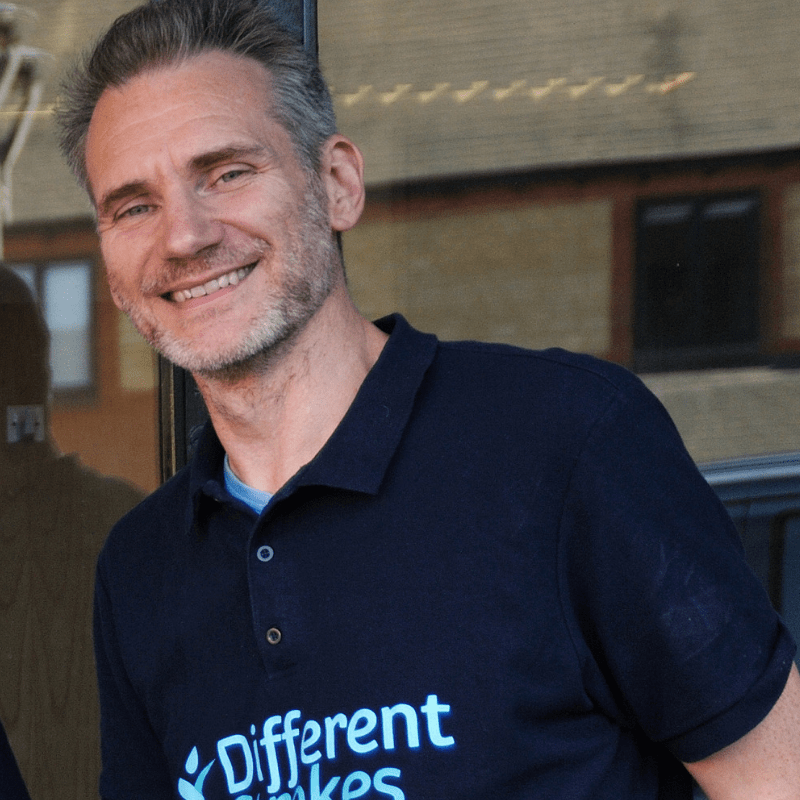 CEO Austin is wearing a Blue Different Strokes Poloshirt standing in front of a building and smiling.