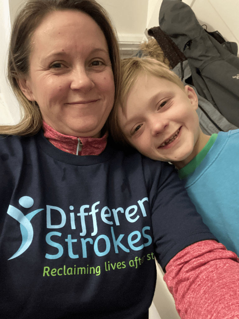 Happy mum wearing a Different Strokes t-shirt with her child happily resting on her shoulder, an example of the families that are supported by donating monthly to Different Strokes