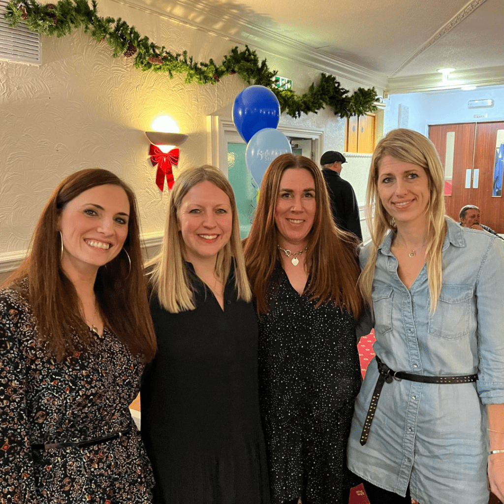 Joanne and three female friends are standing in the function room of a pub embracing and smiling at the camera.
