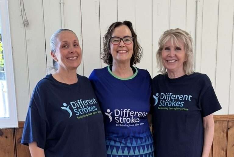 Volunteers Sharon, Lisa, and Jackie standing together and smiling wearing their Different Strokes t-shirts