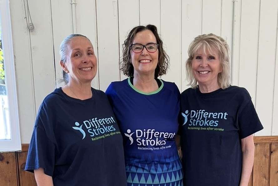 Volunteers Sharon, Lisa, and Jackie standing together and smiling wearing their Different Strokes t-shirts