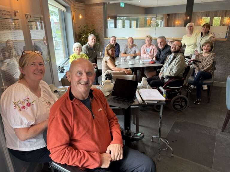 A group photo of members of the Bolton peer support group, with 11 individuals all smiling.