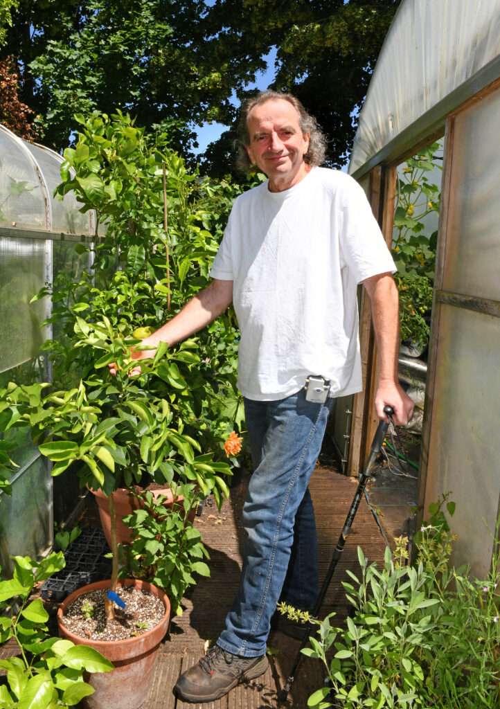 A male with a white tshirt on jeans is enjoying his garden. He has a stick and an Odstock Medical Functional Electrical Simulation device on his leg